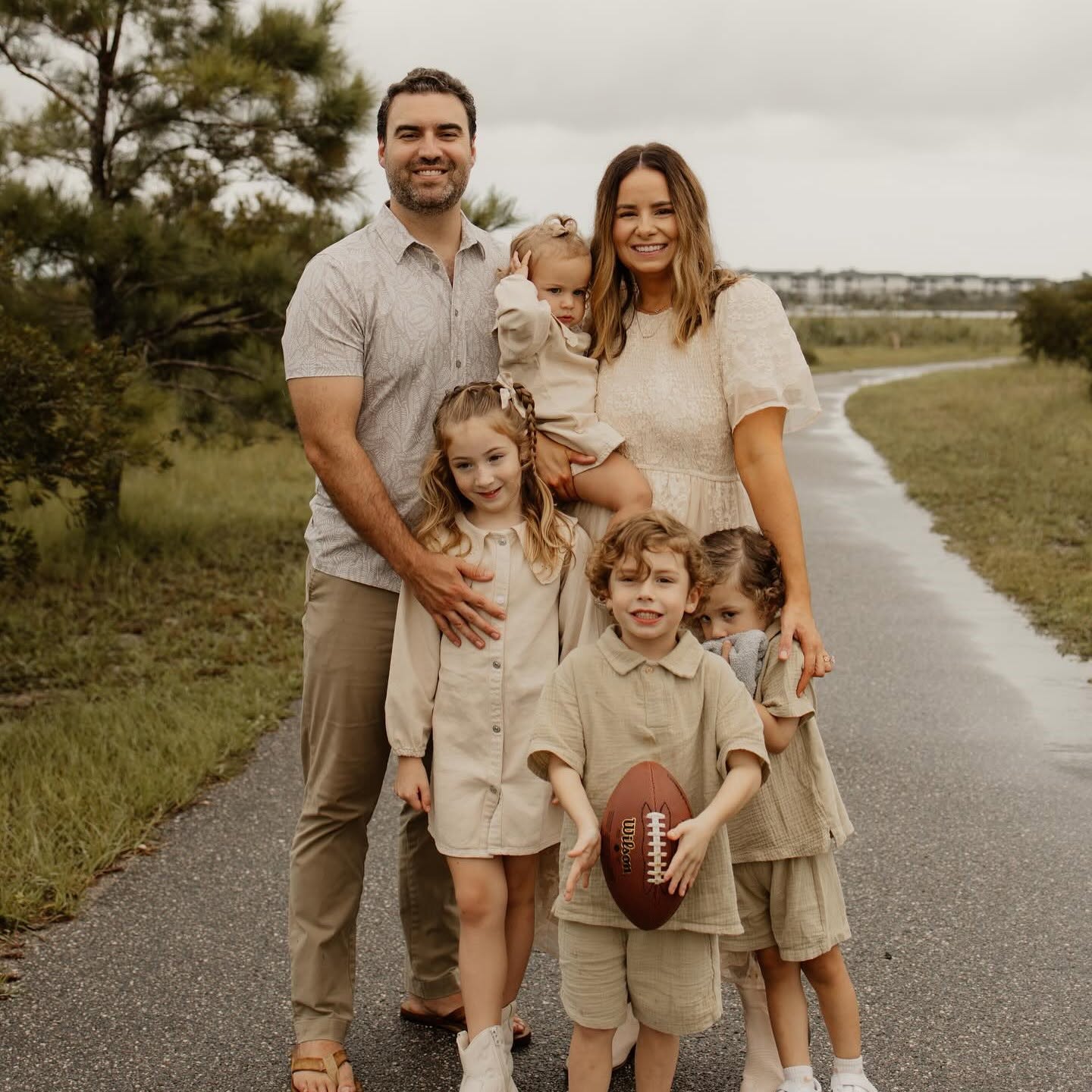 A family stands together on a quiet country path, smiling warmly.
