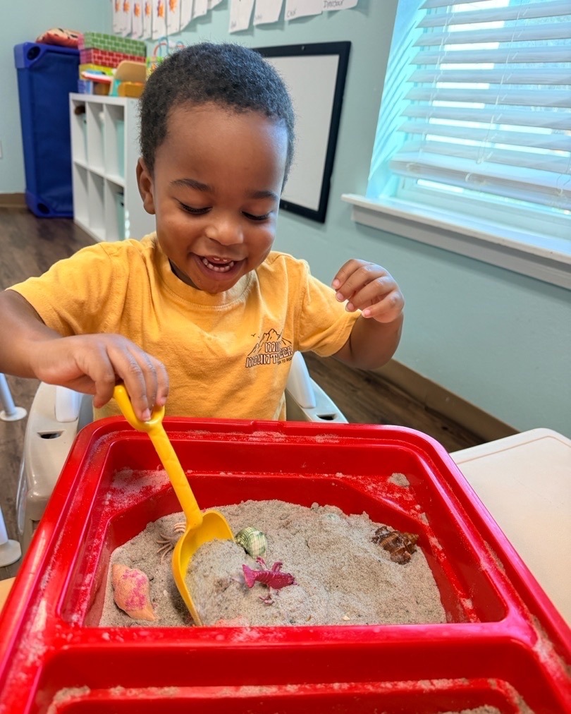 A boy in a yellow shirt exploring a red sensory bin at Tadpole Prep.
